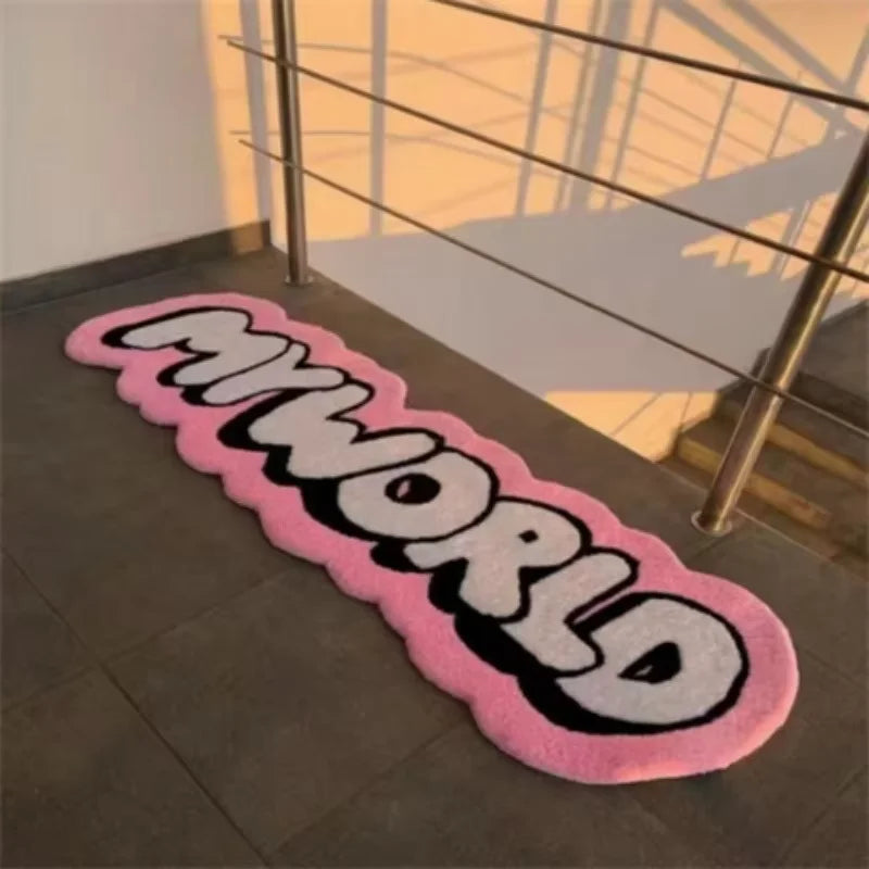 A pink and black mat rug with the word MYWORLD printed on it placed on a dark floor.