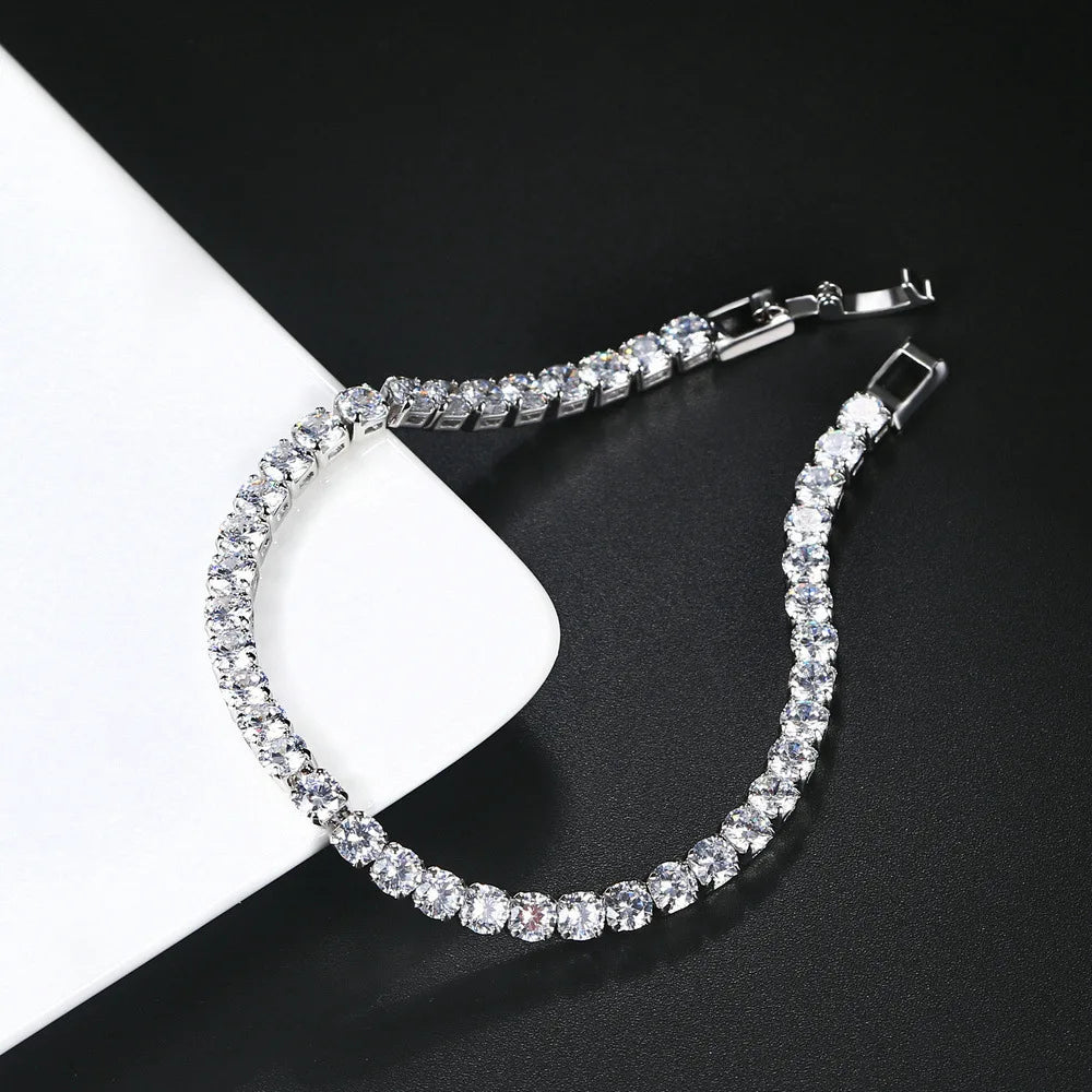 A close-up shot of a diamond tennis bracelet with a silver clasp resting on a white card against a dark background.