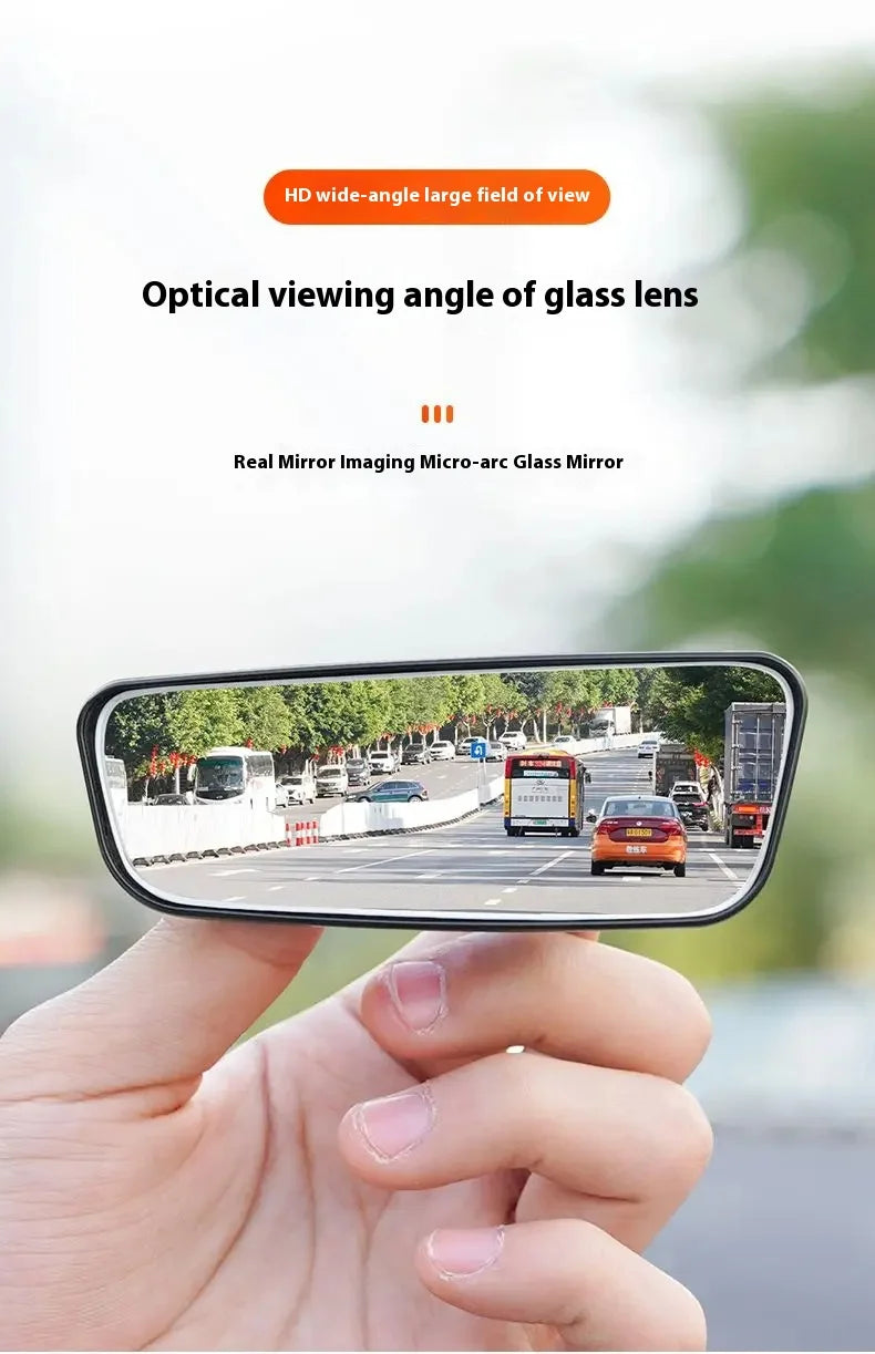 A hand holds a black glass lens mirror showing a wide-angle view of a road with cars and trees.