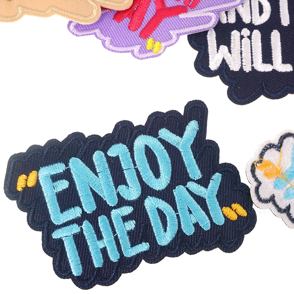 A collection of embroidered iron-on patches featuring colorful text and floral designs on dark fabric.