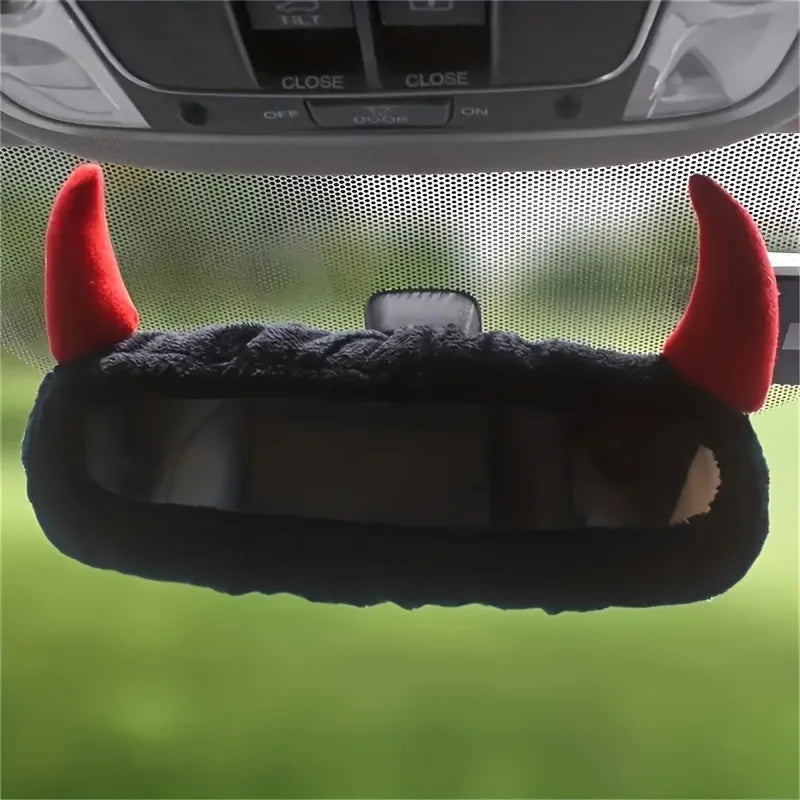A black devil horn rearview mirror cover with red accents shown against a green background.