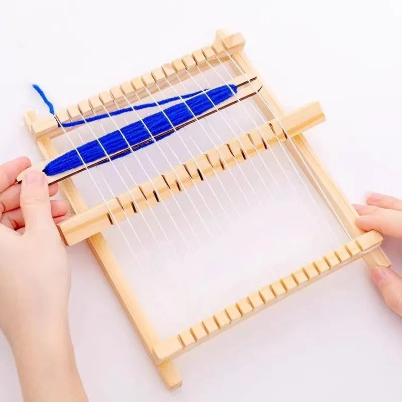 Hands are assembling a compact wooden weaving loom kit with blue threads and wooden strips.