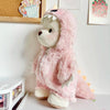 A pink fuzzy teddy bear doll wearing a dinosaur jumpsuit outfit.