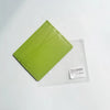 A lime green genuine leather slim card holder wallet placed on a clear plastic background.