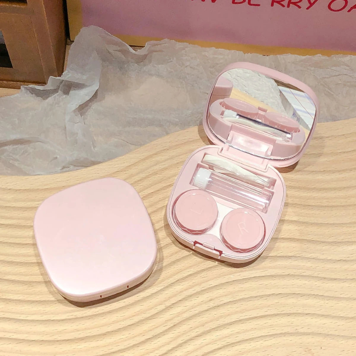 A pink compact contact lens travel case is shown open, revealing storage compartments and a clear lid.