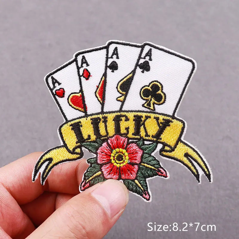A hand holds an embroidered lucky playing card banner featuring aces and a heart, with a decorative floral element.