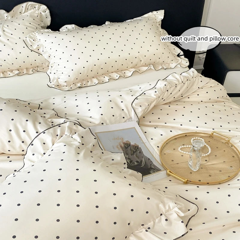 A set of three white bedding pillows and a duvet cover with a black dot print, displayed on a bed.
