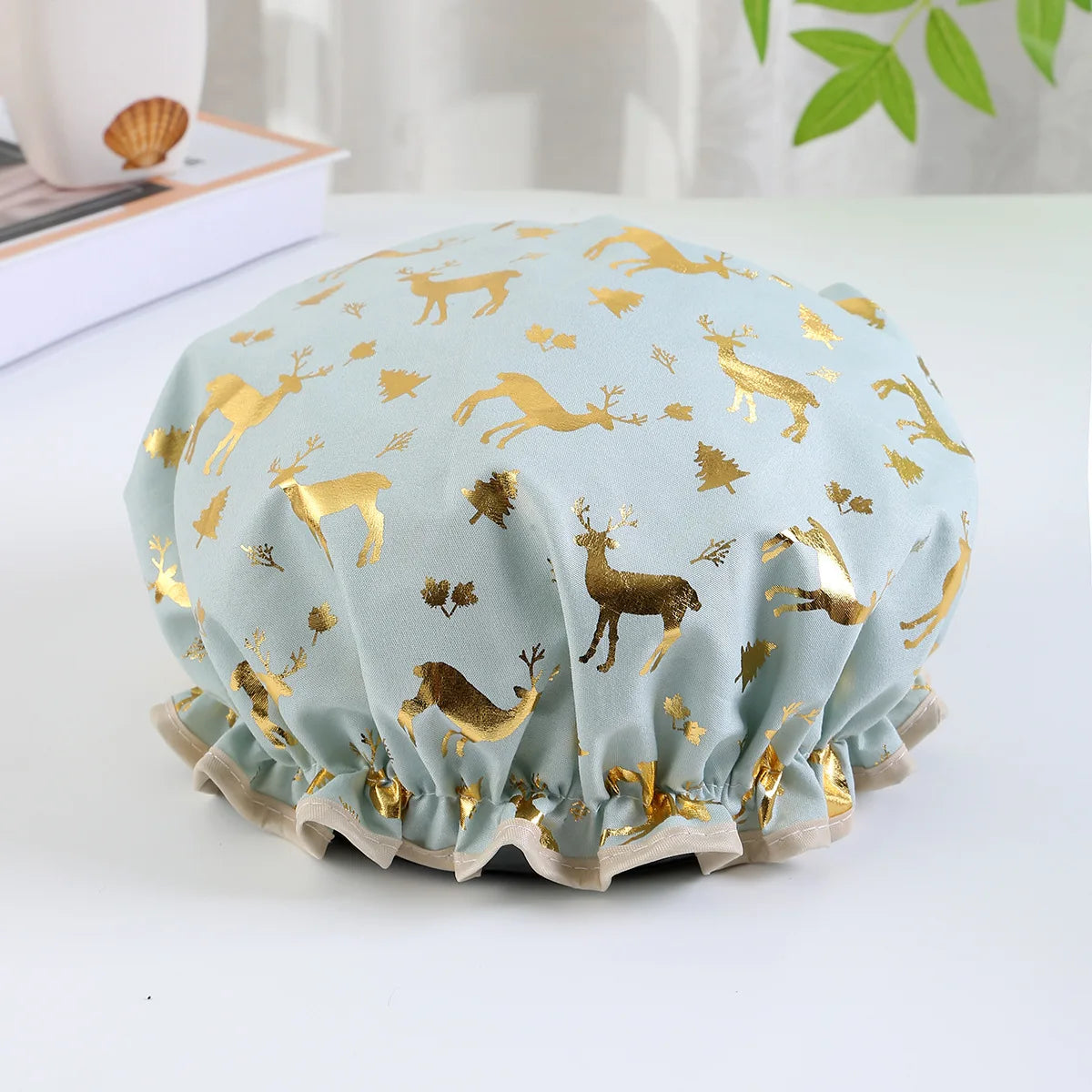 Light blue reusable elastic shower cap patterned with gold deer and foliage designs