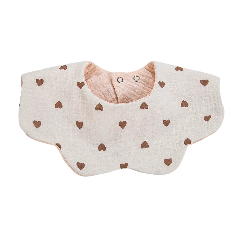 A light beige muslin cotton baby bib with a snap closure and small brown heart embroidery.