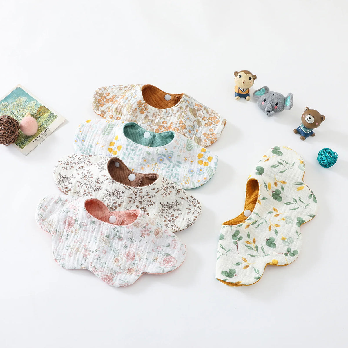 A collection of six-layer cotton baby feeding bibs in various floral patterns and a small stuffed animal