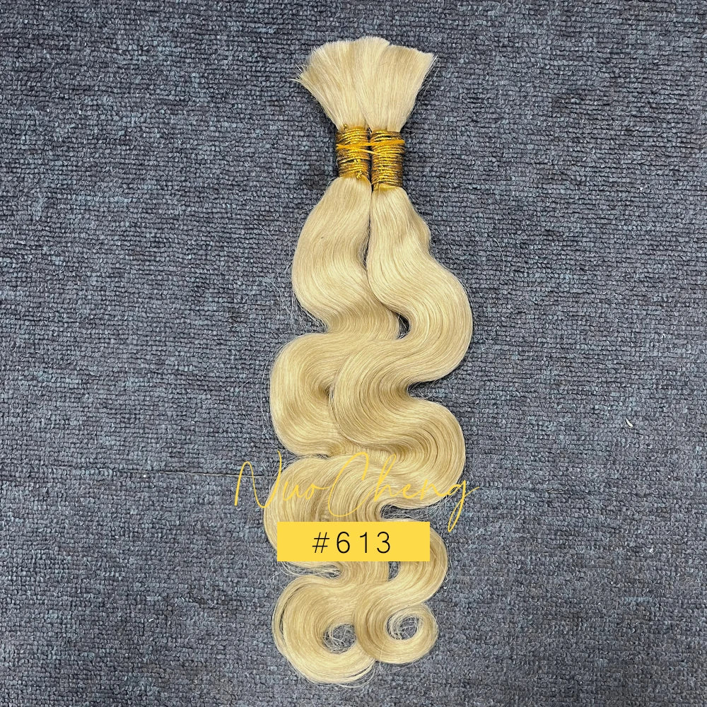 Un paquet de cheveux humains ondulés blonds tressés avec un fil d'or, présenté sur un tissu gris foncé.