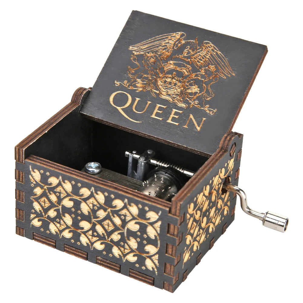 A dark wooden music box with gold accents and an engraved crown design, featuring a hand crank mechanism.