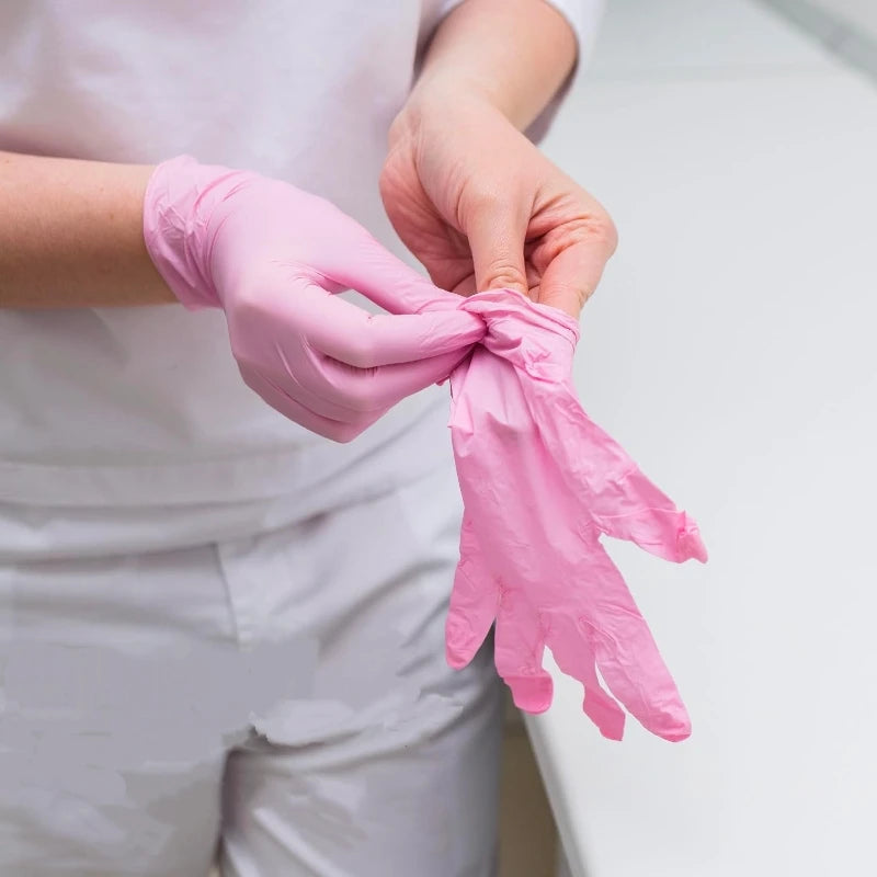 A person is putting on pink nitrile disposable gloves for a medical or food-related task.