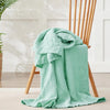 A light mint green muslin cotton blanket draped over a wooden chair in bright natural light.