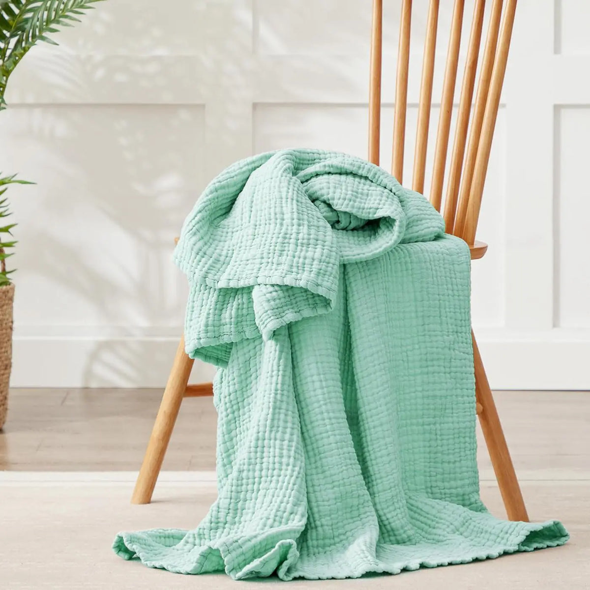 A light mint green muslin cotton blanket draped over a wooden chair in bright natural light.