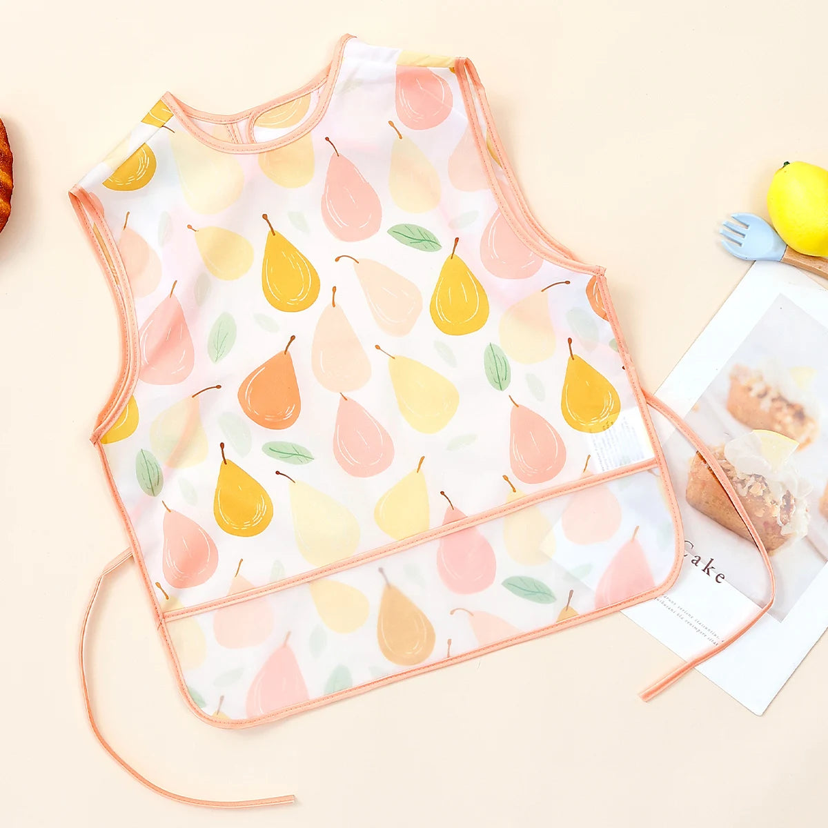 A pink and yellow patterned waterproof baby feeding bib with a sleeveless design featuring fruit shapes.