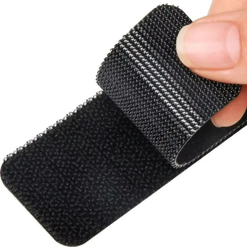A close-up of a black double-sided adhesive carpet and mat fixing patch being held by a hand.