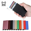 A hand holds a black slim metal RFID blocking card holder with pop-up design next to a row of various colored cards.