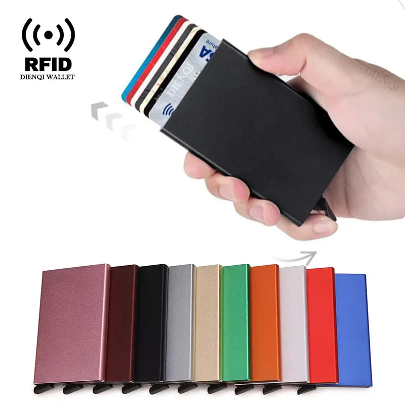 A hand holds a black slim metal RFID blocking card holder with pop-up design next to a row of various colored cards.