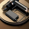 A black cordless handheld vacuum cleaner with a hose and charging cable resting on a round wooden surface.