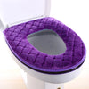 Tapa protectora impermeable de color púrpura para asiento de inodoro instalado en un inodoro blanco.