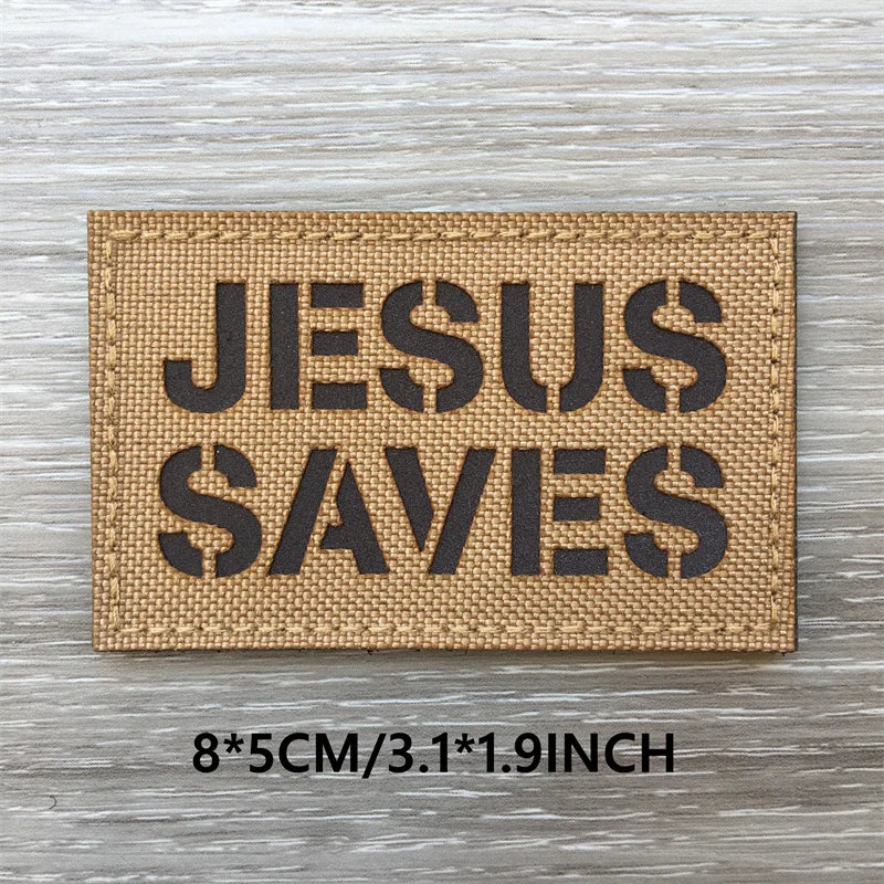 A rectangular tan woven patch with black text reading JESUS SAVES on a weathered wooden surface.