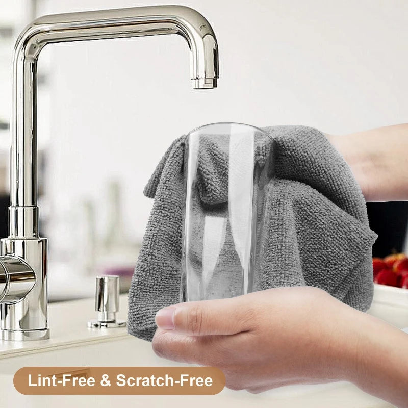 A hand is wiping a glass faucet with a gray microfiber cleaning wipe.