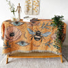 A bohemian jacquard woven throw blanket featuring an orange background with floral patterns, eyes, and a bee motif.