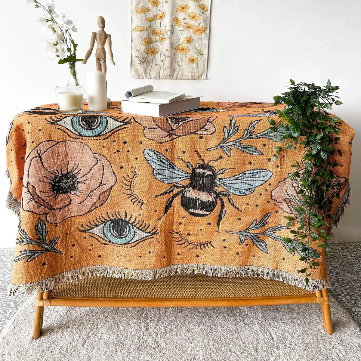 A bohemian jacquard woven throw blanket featuring an orange background with floral patterns, eyes, and a bee motif.