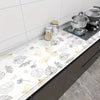 Marble peel-and-stick wallpaper used as a backsplash on a dark kitchen countertop with stainless steel pots.