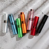 Un set de tres atomizadores de perfume coloridos en plata, azul, naranja, rosa, rojo y negro, mostrados sobre una superficie 