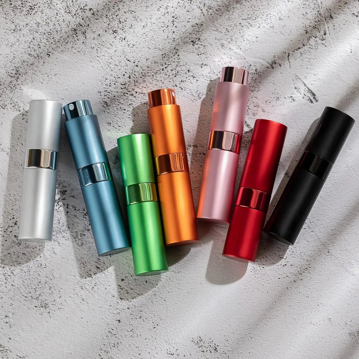 Un set de tres atomizadores de perfume coloridos en plata, azul, naranja, rosa, rojo y negro, mostrados sobre una superficie 