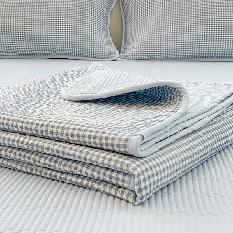 A stack of white and gray quilted linen fabric covers resting on a white bedspread.
