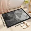 A rectangular gray and black bathroom mat with a geometric pattern is shown next to wooden slippers.