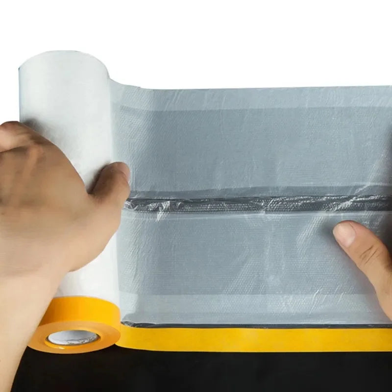 A hand is holding a roll of static-cling clear plastic sheeting for painting and protection.