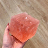 A hand holds a translucent pink frosted matte jumbo cheese stress ball against a wooden background.