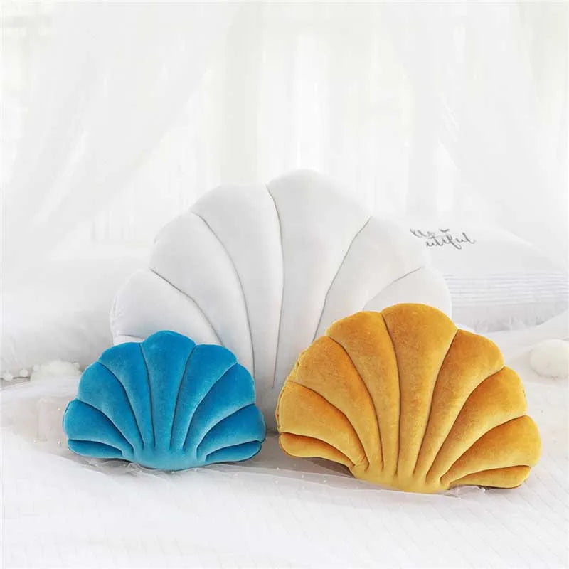 A pair of decorative velvet shell print throw pillows in blue and gold resting on a white surface.
