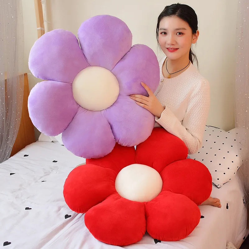 A woman is holding a large purple and red sunflower plush pillow on a white bed.