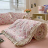 A pink floral washed cotton gauze summer quilt rolled up on a pink bed.
