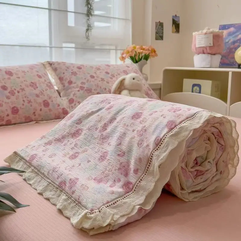 A pink floral washed cotton gauze summer quilt rolled up on a pink bed.