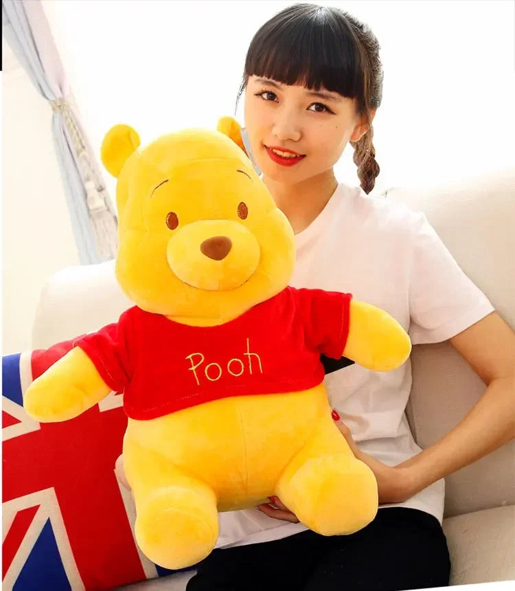 A young woman is holding a yellow Winnie the Pooh plush toy with a red shirt.