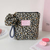 A leopard print cosmetic bag with a gold zipper and gray strap resting on a white surface.