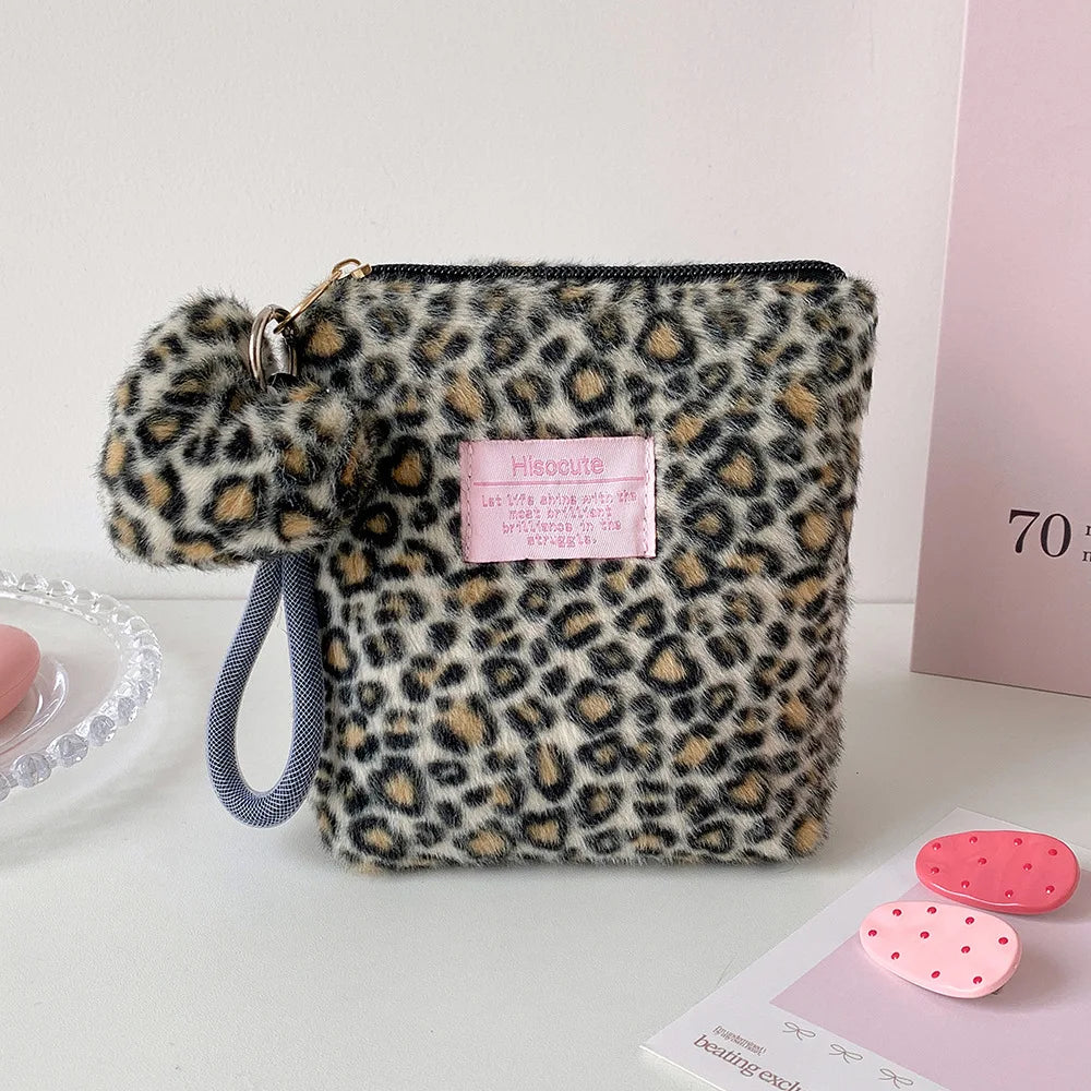 A leopard print cosmetic bag with a gold zipper and gray strap resting on a white surface.