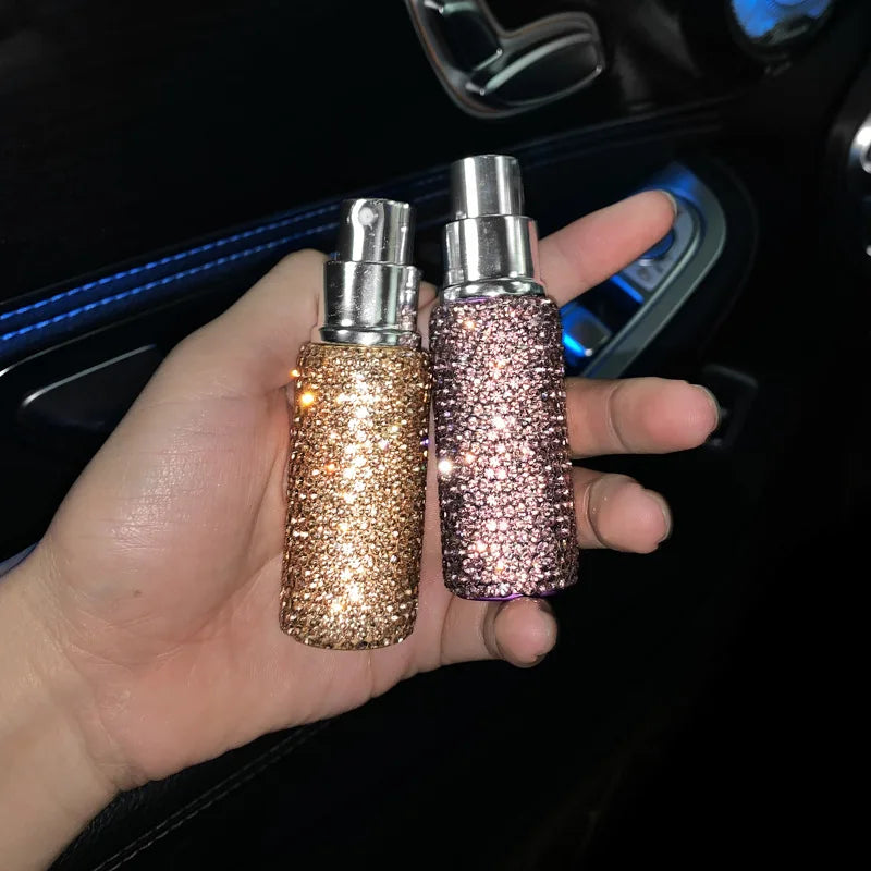 A hand holds two glass perfume atomizers, one gold and one pink, with silver spray tops.