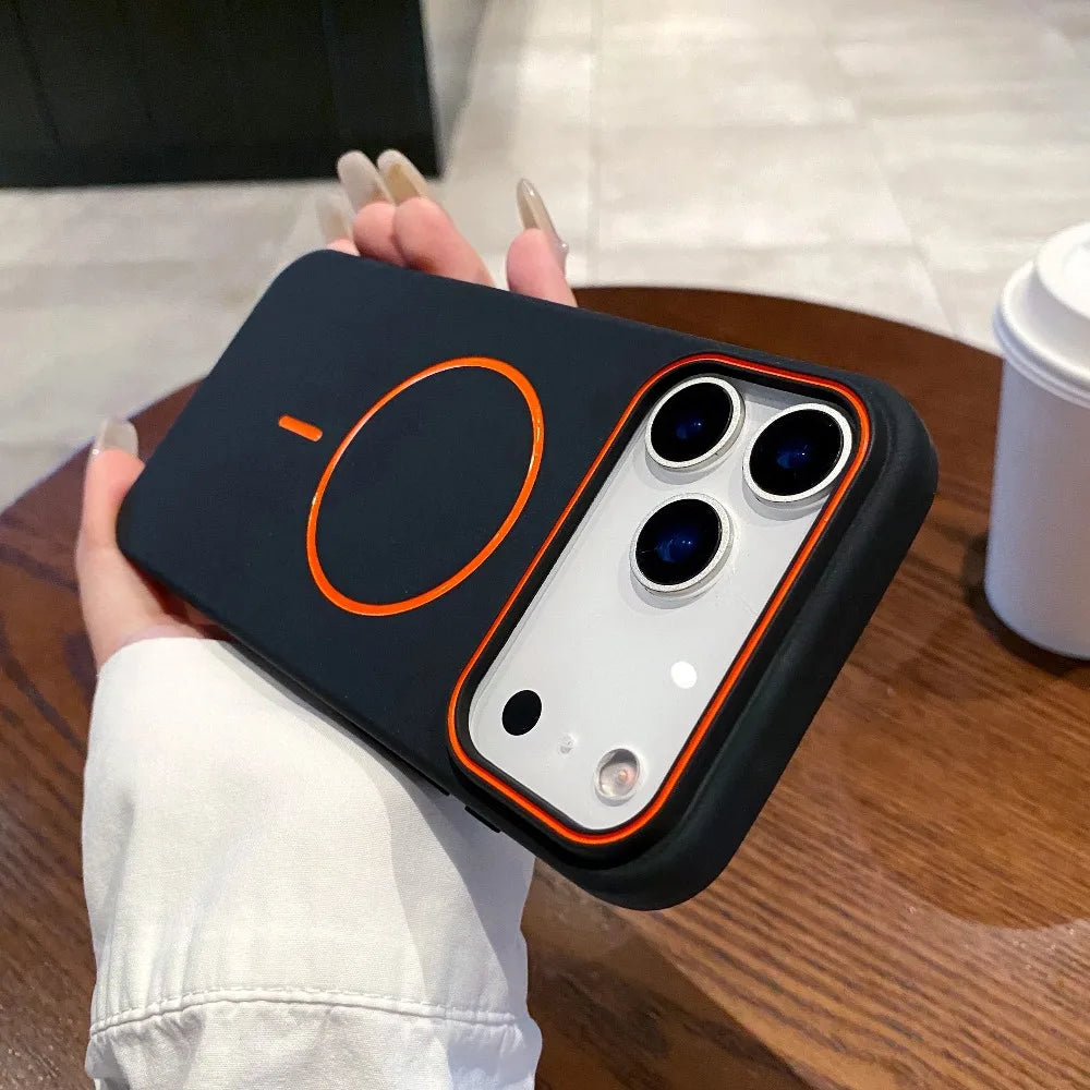 A hand holds a dark phone case with an orange circular design and MagSafe support on a wooden surface.