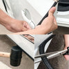 Hands are installing a U-shaped rubber edge trim with a metal core onto a car door using a tool.