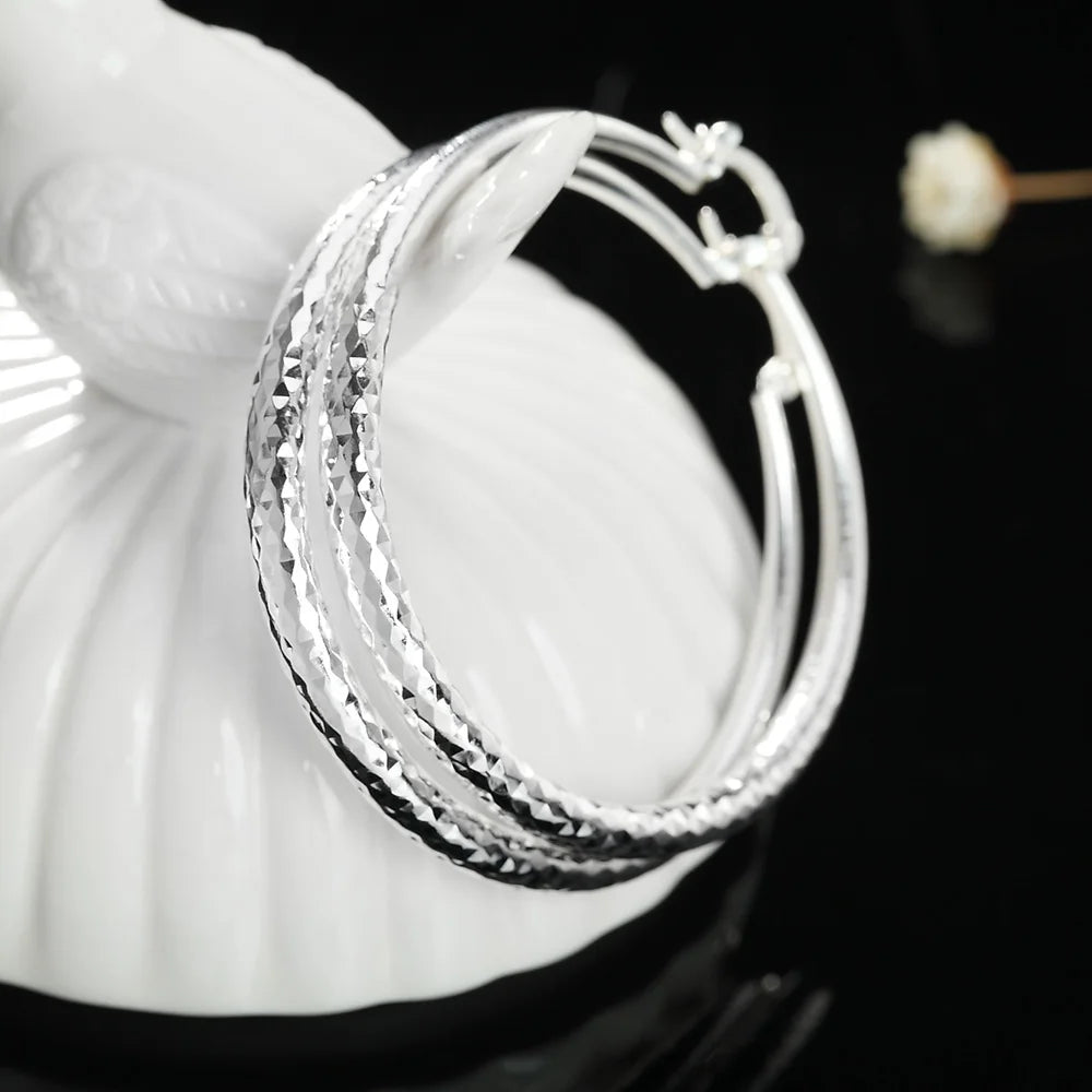Boucles d'oreilles en anneau argentées posées sur un objet décoratif blanc.