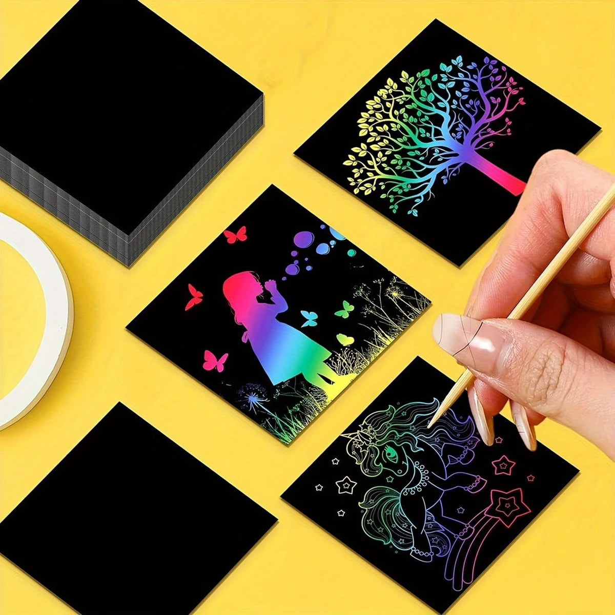 A set of black art paper sheets featuring colorful rainbow designs and a wooden stylus being held by a hand.
