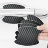 A hand holds a black carbon fiber door handle protector film, showing its textured surface against a silver car door handle.
