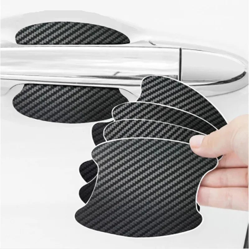 A hand holds a black carbon fiber door handle protector film, showing its textured surface against a silver car door handle.
